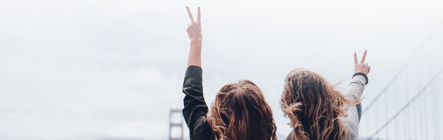 Two women holding up peace signs in front of the Golden Gate Bridge